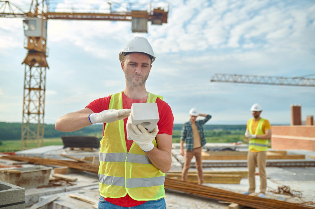удівельник у касці перевіряє якість газоблока на будівельному майданчику